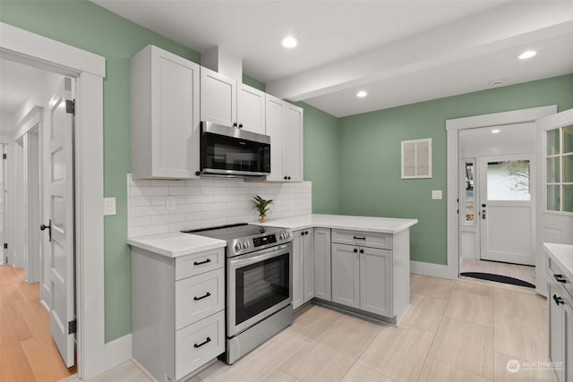 kitchen with stainless steel appliances, light hardwood / wood-style flooring, backsplash, kitchen peninsula, and white cabinets