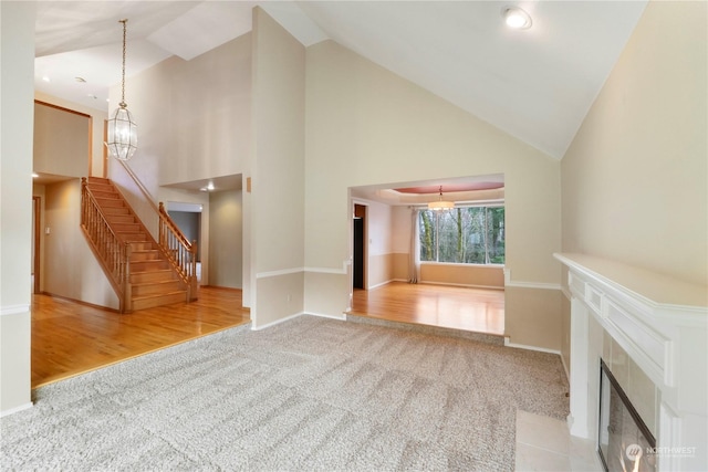 unfurnished living room featuring carpet, a fireplace, high vaulted ceiling, and a chandelier