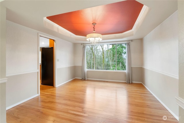 unfurnished room with a tray ceiling, hardwood / wood-style flooring, and a notable chandelier