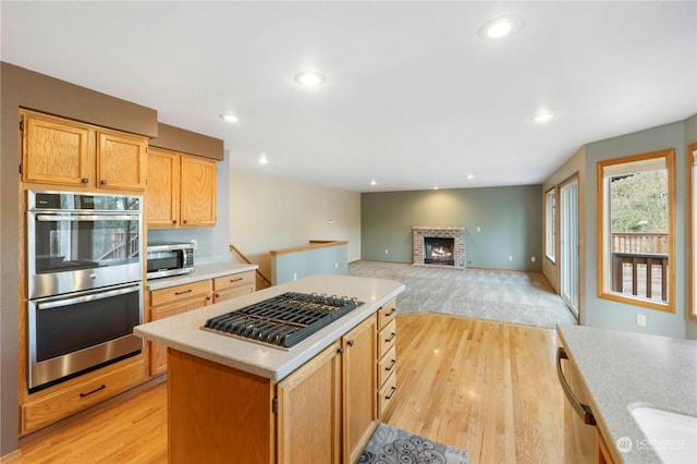 kitchen featuring appliances with stainless steel finishes, a fireplace, light brown cabinetry, a kitchen island, and light wood-type flooring