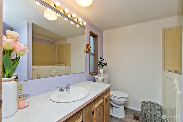 bathroom with washing machine and clothes dryer, toilet, vanity, and hardwood / wood-style flooring