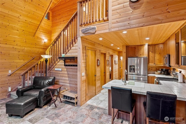 kitchen with tile countertops, wood walls, wooden ceiling, kitchen peninsula, and stainless steel appliances