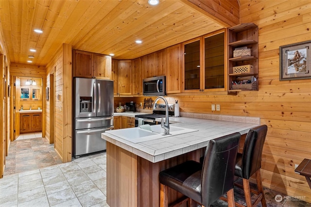 kitchen with kitchen peninsula, appliances with stainless steel finishes, a kitchen bar, and wood walls