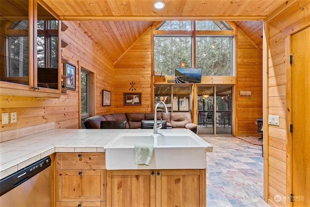 kitchen featuring tile countertops, wood walls, stainless steel dishwasher, and lofted ceiling