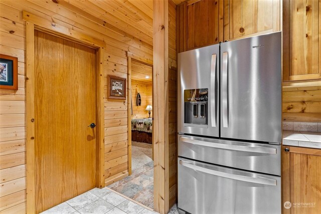 kitchen with stainless steel fridge with ice dispenser, light tile patterned floors, tile counters, and wooden walls