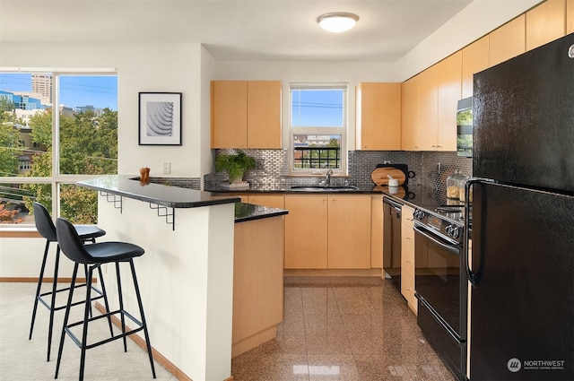 kitchen featuring a kitchen bar, sink, black appliances, and light brown cabinets