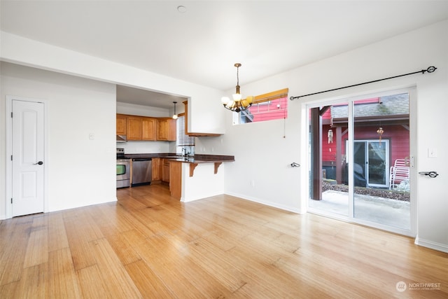 kitchen with a kitchen bar, appliances with stainless steel finishes, kitchen peninsula, pendant lighting, and light hardwood / wood-style floors