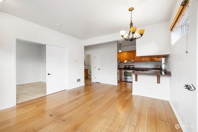 2606 Peach Ct Unit B, Port Angeles, WA 98363 - kitchen with stainless steel stove, dark countertops, a chandelier, light wood-style flooring, and brown cabinetry