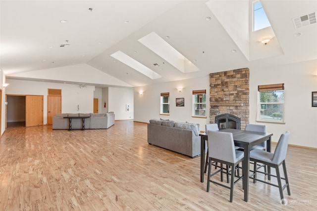 dining space featuring light hardwood / wood-style floors, a fireplace, high vaulted ceiling, and a skylight