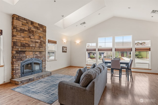 living room with a fireplace, hardwood / wood-style floors, high vaulted ceiling, and a skylight