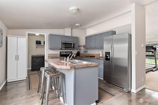 kitchen with stainless steel appliances, vaulted ceiling, sink, a center island with sink, and washer / clothes dryer