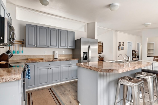 kitchen featuring appliances with stainless steel finishes, dark hardwood / wood-style flooring, gray cabinetry, sink, and an island with sink