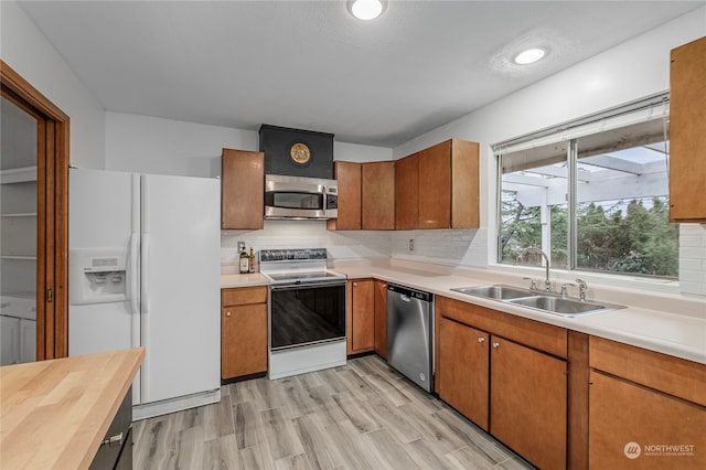 kitchen with stainless steel appliances, a sink, light wood-type flooring, backsplash, and brown cabinetry