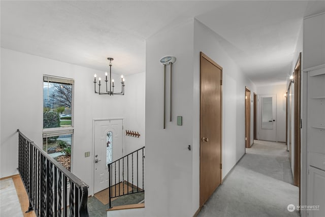 hallway with light carpet, a notable chandelier, and an upstairs landing