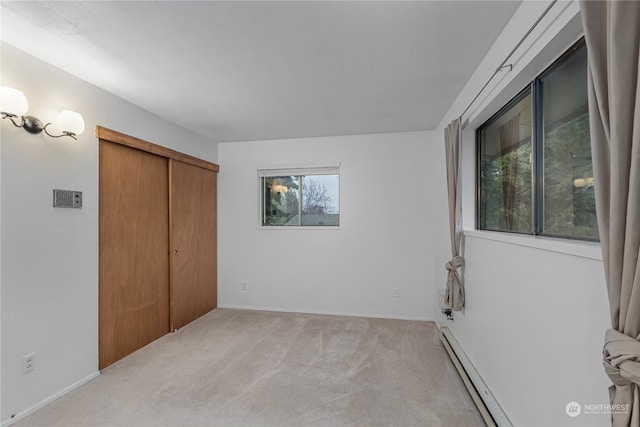 unfurnished bedroom featuring baseboards, baseboard heating, a closet, and light colored carpet