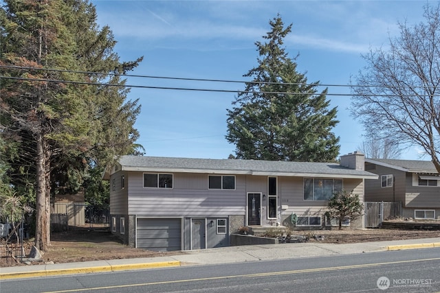 split foyer home with a garage, a chimney, and fence