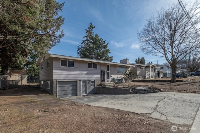 bi-level home with an attached garage, fence, and concrete driveway