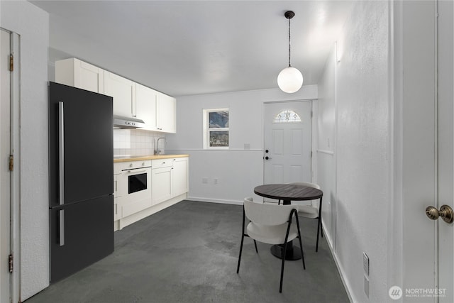 kitchen featuring white cabinets, white oven, freestanding refrigerator, under cabinet range hood, and backsplash