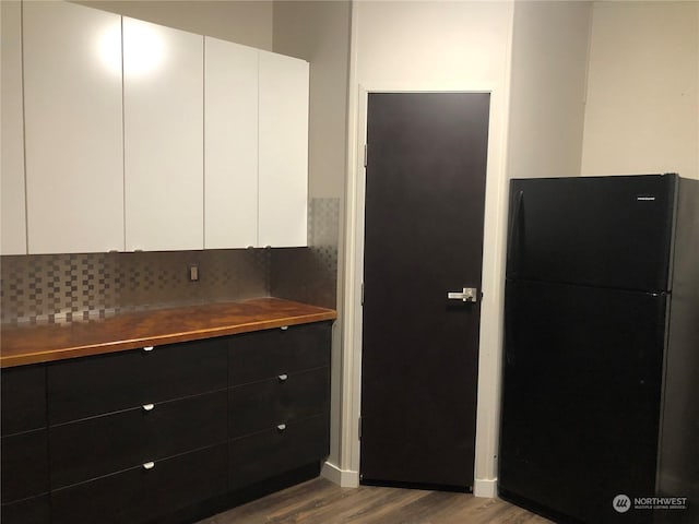 kitchen with white cabinetry, black fridge, and light hardwood / wood-style floors