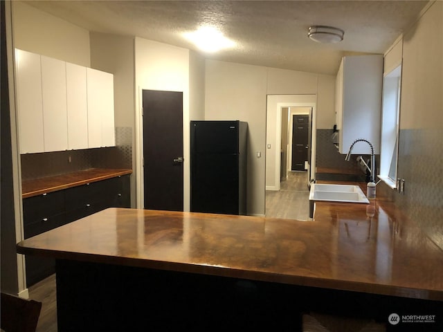 kitchen with light wood-type flooring, a textured ceiling, vaulted ceiling, sink, and white cabinets