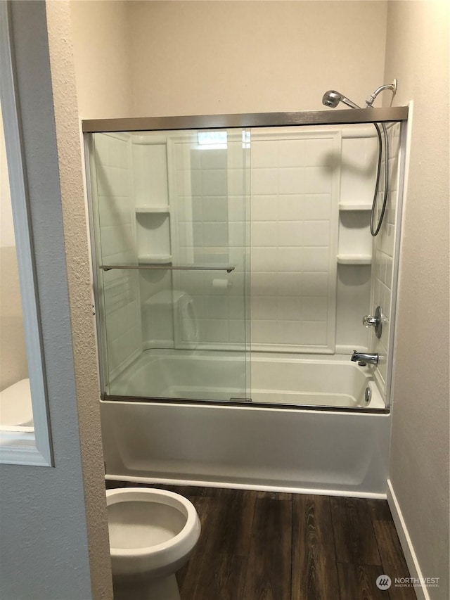 bathroom featuring toilet, wood-type flooring, and combined bath / shower with glass door