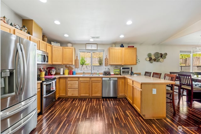 kitchen with kitchen peninsula, appliances with stainless steel finishes, a breakfast bar, and dark wood-type flooring