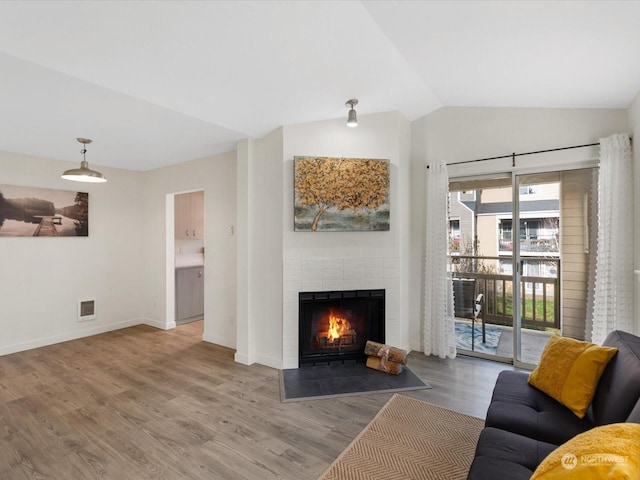 living room with hardwood / wood-style floors, a brick fireplace, and vaulted ceiling