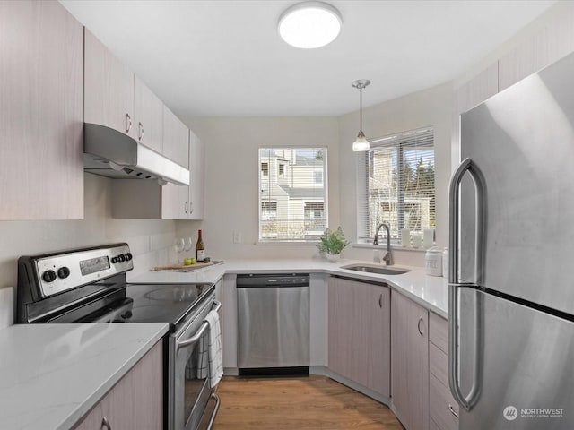 kitchen featuring sink, light wood-type flooring, decorative light fixtures, light stone counters, and stainless steel appliances