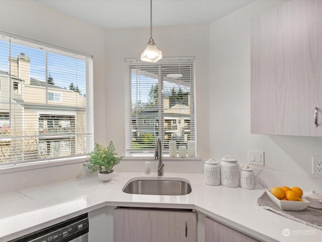 kitchen featuring dishwashing machine, decorative light fixtures, sink, and light brown cabinetry