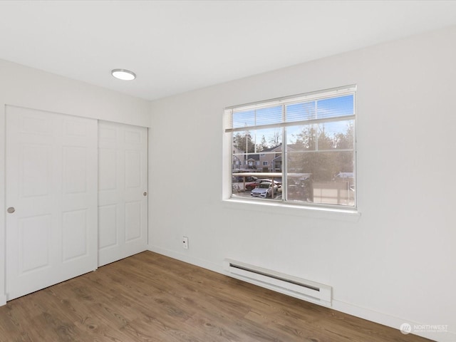 unfurnished bedroom with wood-type flooring, a closet, and a baseboard heating unit