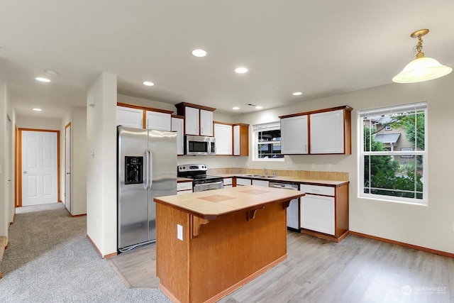 kitchen with appliances with stainless steel finishes, tile countertops, white cabinetry, and decorative light fixtures