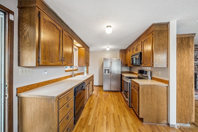 kitchen with appliances with stainless steel finishes, light hardwood / wood-style floors, sink, and a textured ceiling