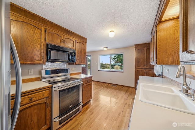 kitchen featuring sink, light wood-type flooring, a textured ceiling, and appliances with stainless steel finishes