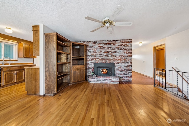 unfurnished living room featuring sink, a textured ceiling, a wood stove, light wood-type flooring, and ceiling fan