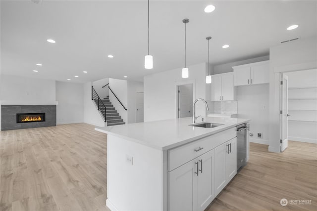 kitchen with sink, a tile fireplace, a center island with sink, white cabinetry, and hanging light fixtures