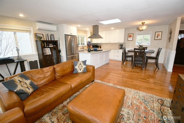 living room with sink, a skylight, light hardwood / wood-style floors, and an AC wall unit