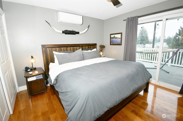 bedroom with ceiling fan, a wall mounted AC, hardwood / wood-style floors, and access to exterior