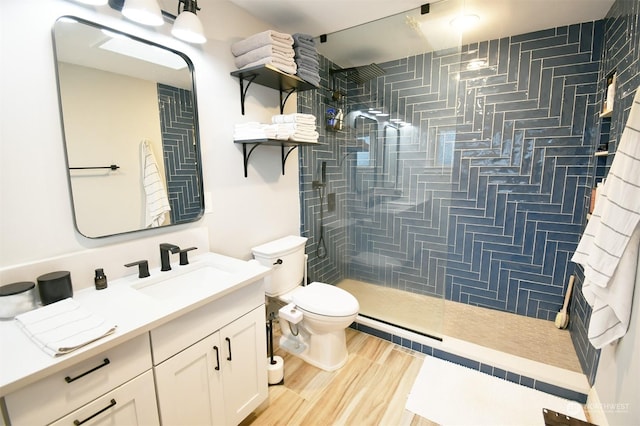 bathroom featuring toilet, a tile shower, wood-type flooring, and vanity