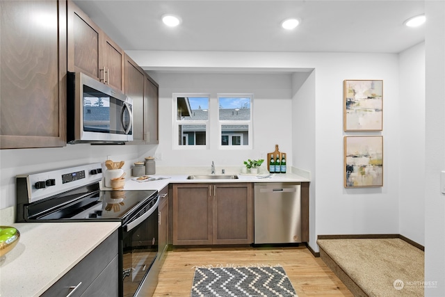 kitchen featuring stainless steel appliances, sink, dark brown cabinetry, and light wood-type flooring