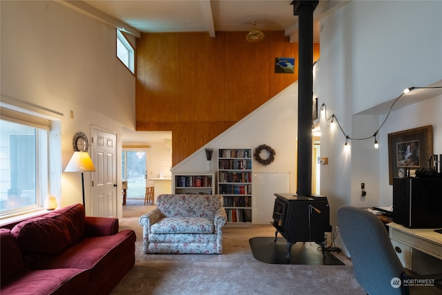 living room featuring carpet, wood walls, a wood stove, a towering ceiling, and beamed ceiling