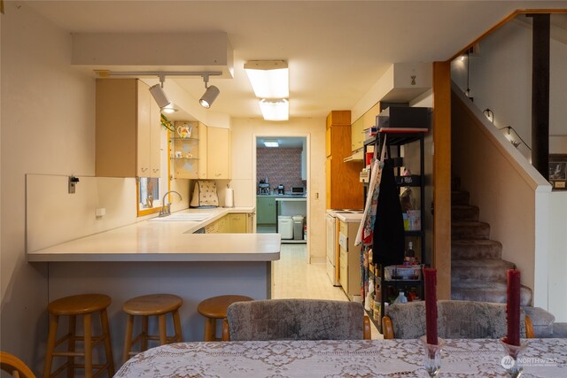 kitchen with kitchen peninsula, a kitchen breakfast bar, backsplash, rail lighting, and sink