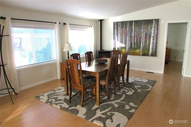 dining area with hardwood / wood-style flooring, lofted ceiling, and a wood stove