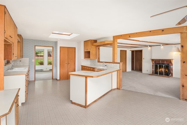 kitchen with kitchen peninsula, backsplash, a skylight, sink, and a fireplace