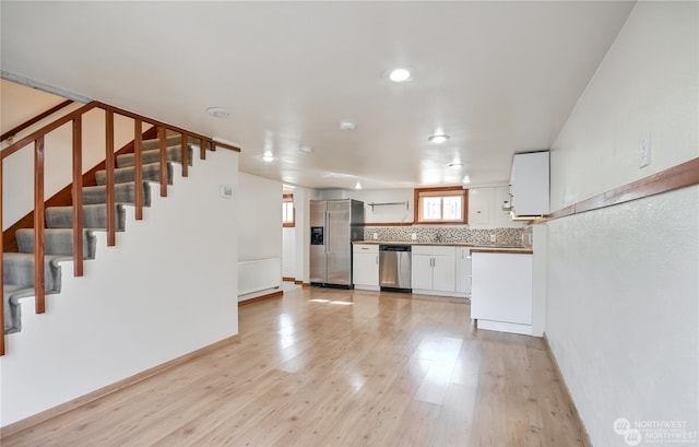 kitchen with backsplash, white cabinetry, light hardwood / wood-style flooring, and appliances with stainless steel finishes