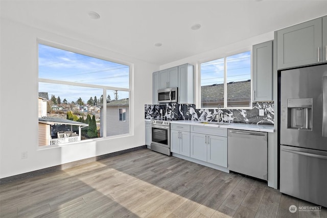 kitchen with light wood-type flooring, backsplash, stainless steel appliances, and gray cabinets