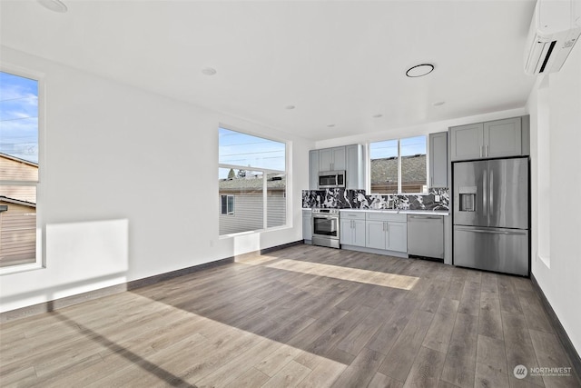 kitchen featuring stainless steel appliances, backsplash, a wall unit AC, gray cabinets, and hardwood / wood-style flooring