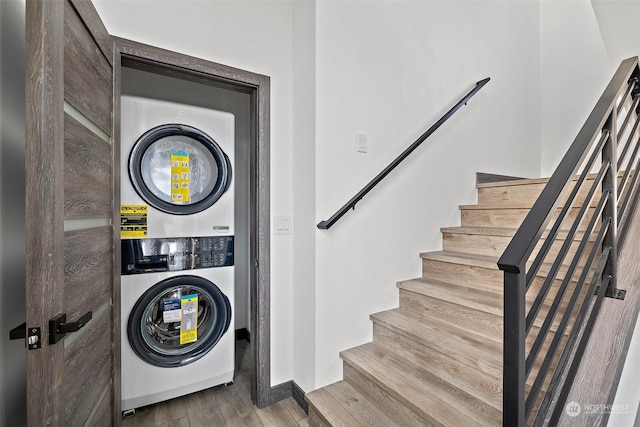 clothes washing area featuring stacked washing maching and dryer and wood-type flooring