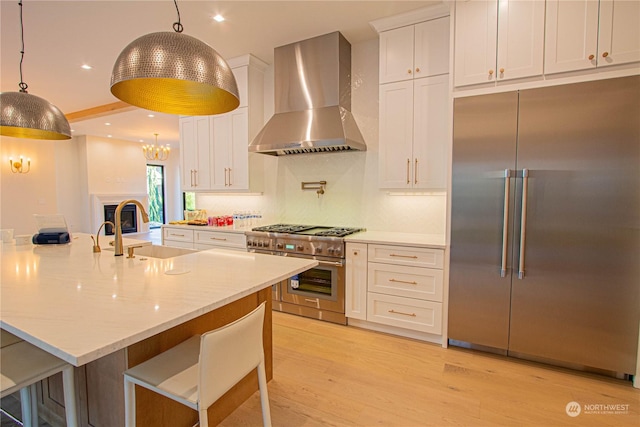 kitchen featuring a kitchen bar, sink, high end appliances, wall chimney range hood, and white cabinets