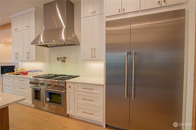 kitchen featuring high end appliances, white cabinetry, light hardwood / wood-style floors, and wall chimney exhaust hood