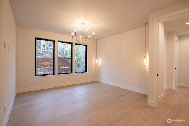 spare room featuring a chandelier and light hardwood / wood-style floors